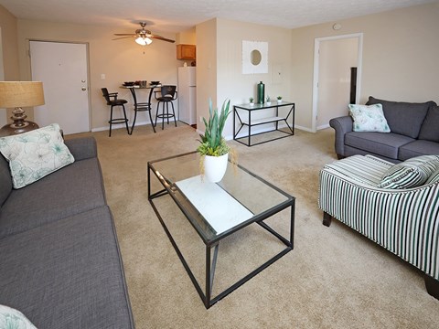 A living room with a grey couch, a black and white striped chair, a glass table, and a dining table with chairs.